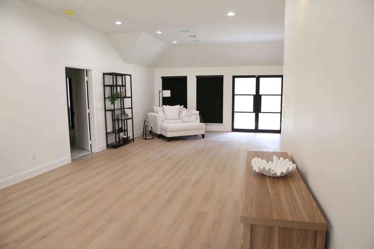 Long bright room with light wood-look floors, white walls and black-framed French doors