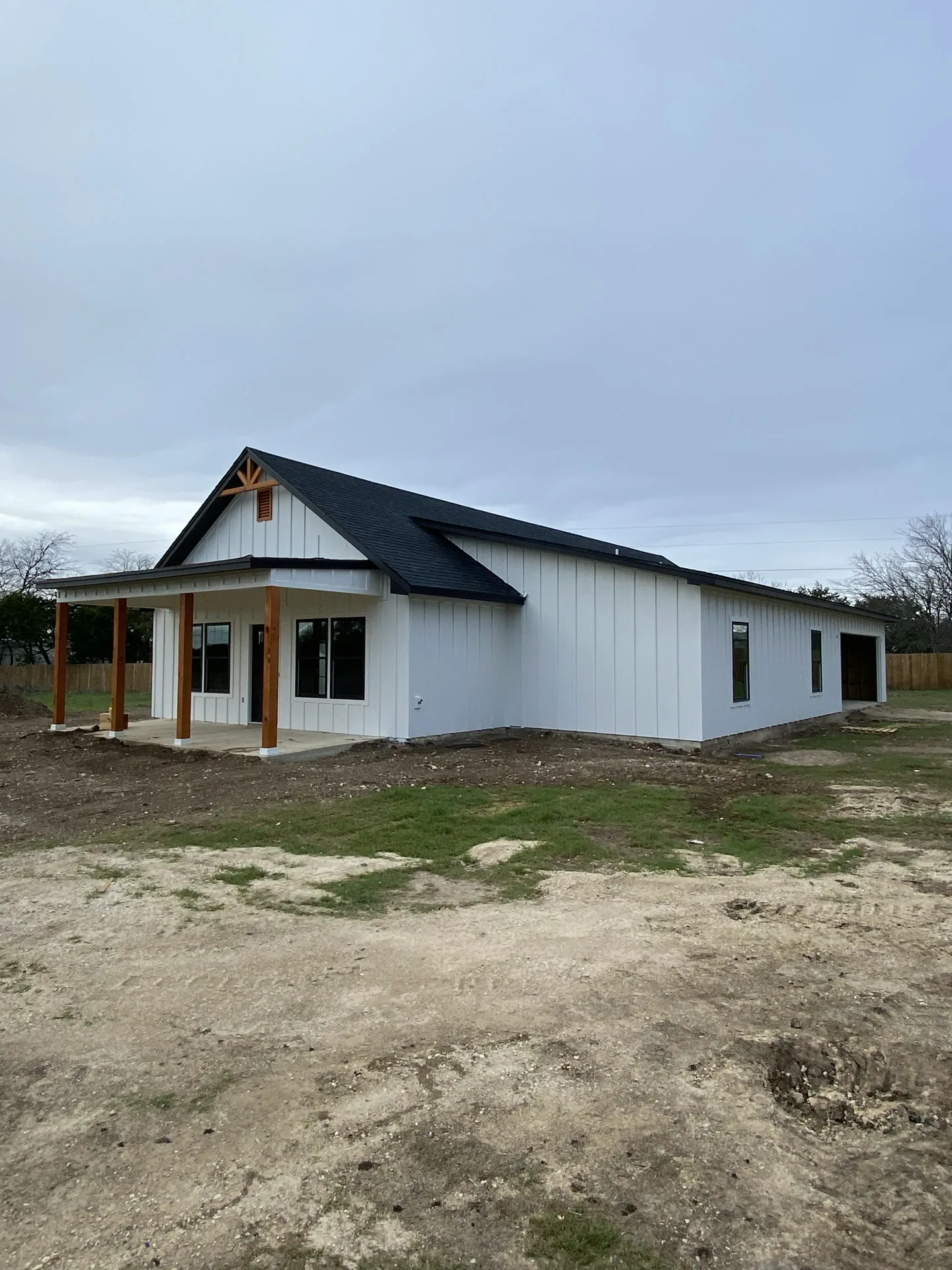 New white board-and-batten farmhouse with a black roof and wood-tone porch posts