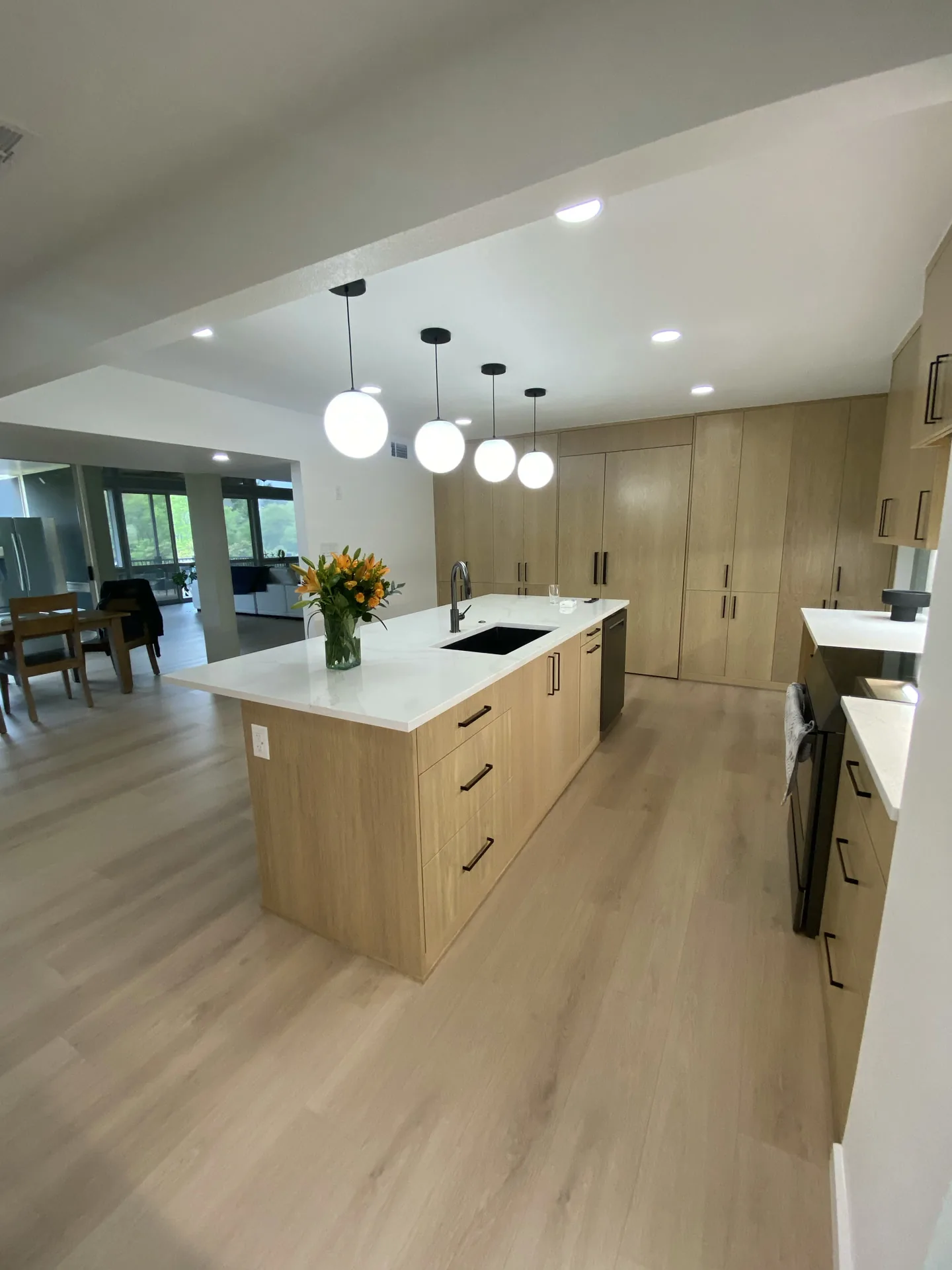 Modern kitchen with light wood-tone cabinets, a long white island and globe pendant lights