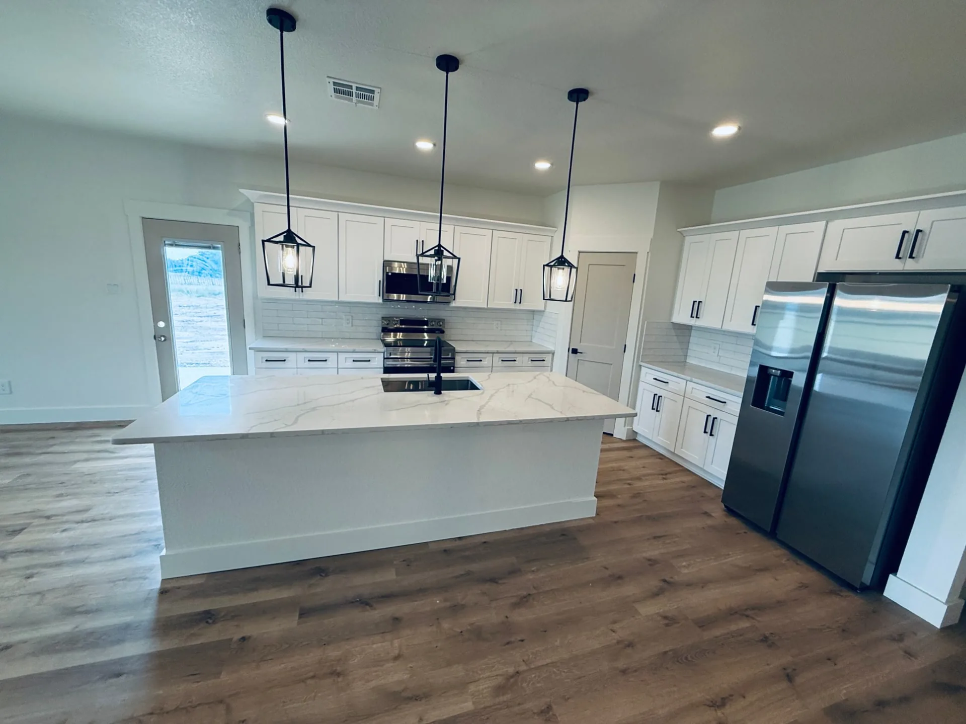 White shaker kitchen with a white stone-look island, black lantern pendants and steel-colored appliances