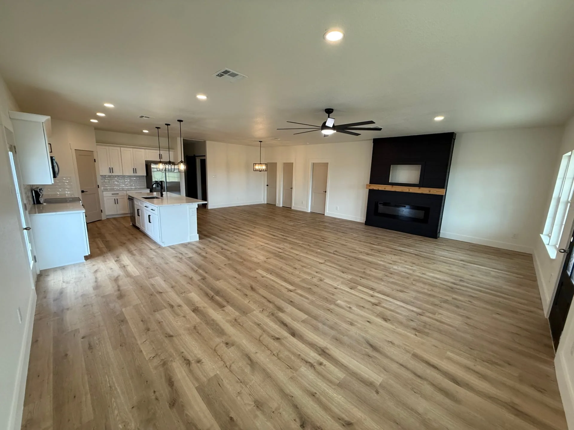 Open living room and kitchen with wood-look floors and a black plank-style fireplace wall